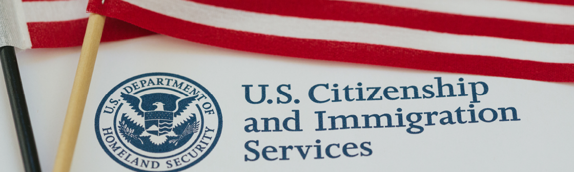 USCIS government agency seal on a document next to two small American flags.