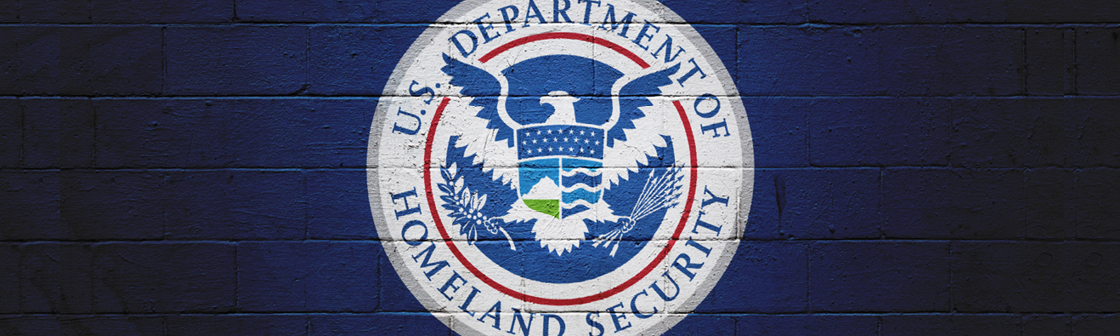 U.S. Department of Homeland Security government agency seal over dark blue brick wall background.
